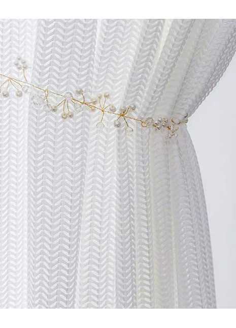 A close-up view of a white, sheer curtain with a decorative gold-colored ribbon or chain attached to it.