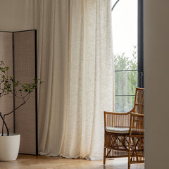 a chair sitting next to a window with a white curtain