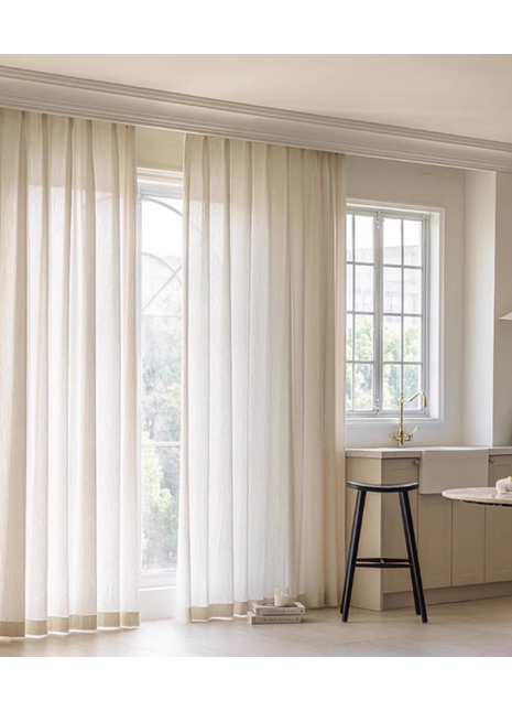 a bright and airy kitchen with a large window, white curtains, and a black stool.