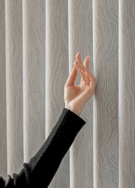 a woman's hand reaching up to a vertical blind