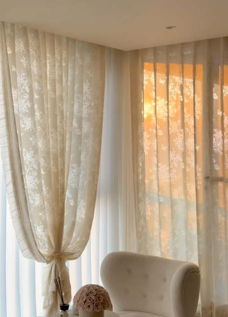 a cozy living room with a plush white armchair, a decorative vase, and a window with sheer curtains.