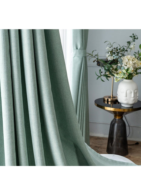 Rideau vert amande texturé retenu par une embrasse dans un salon lumineux, avec table d'appoint et bouquet blanc